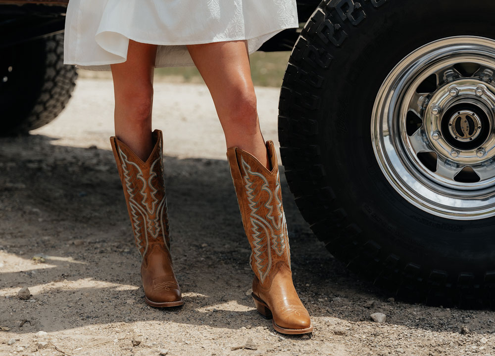 A woman wearing Justin western boots while standing next to a truck.